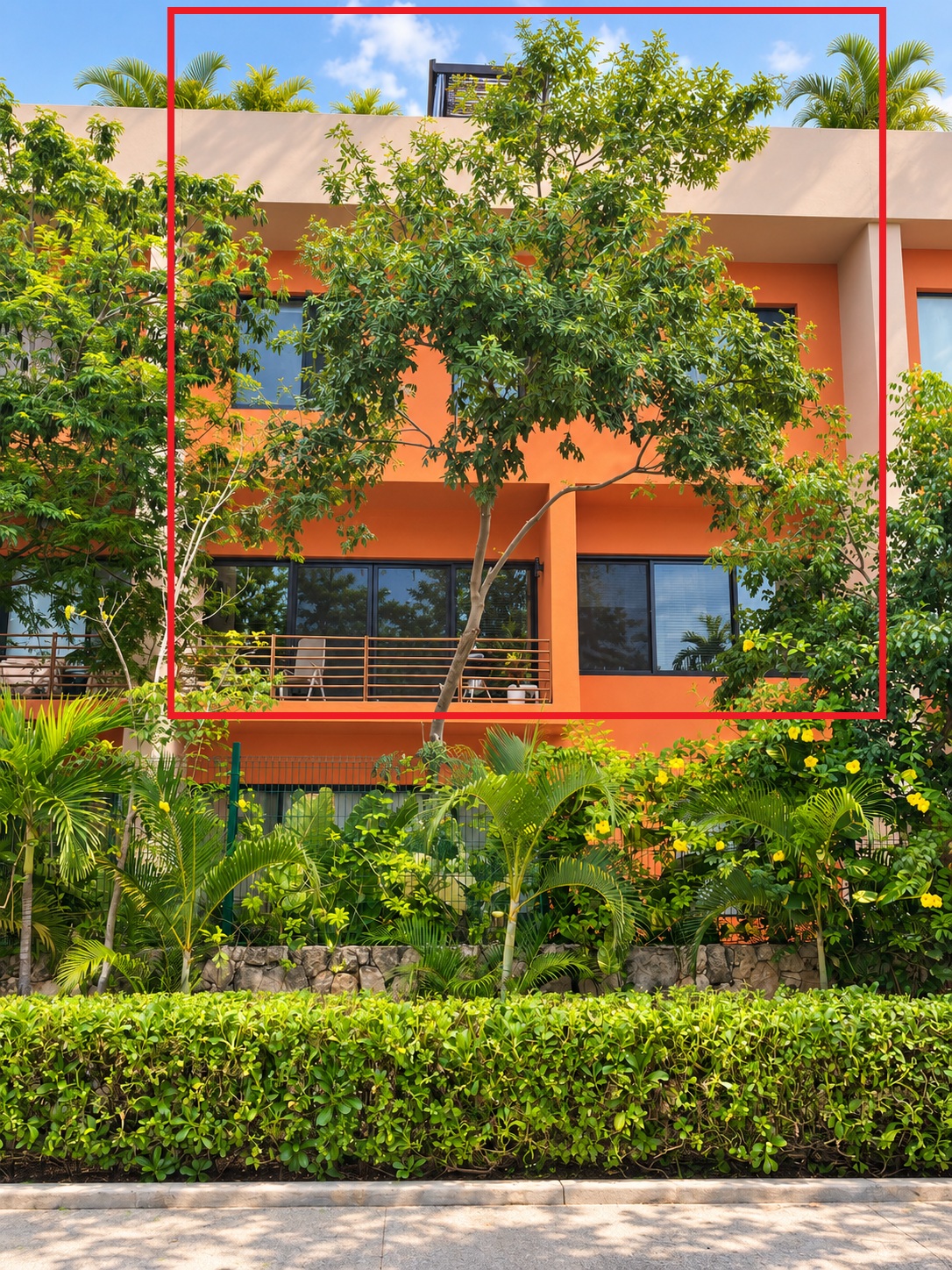 Rear facade of the orange Aleda building seen from the garden, with a red frame around the unit
